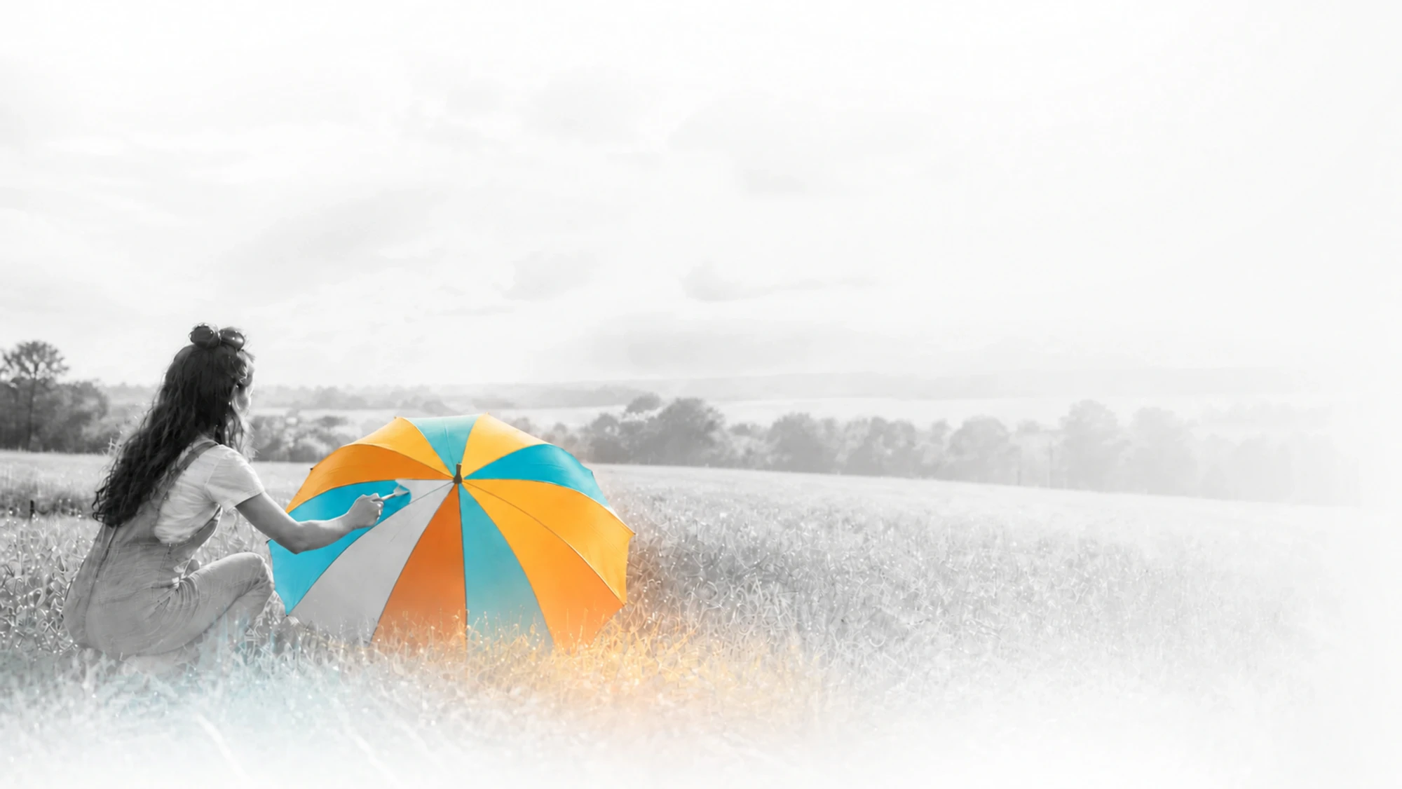 A woman in a monochrome meadow painting a brightly coloured umbrella